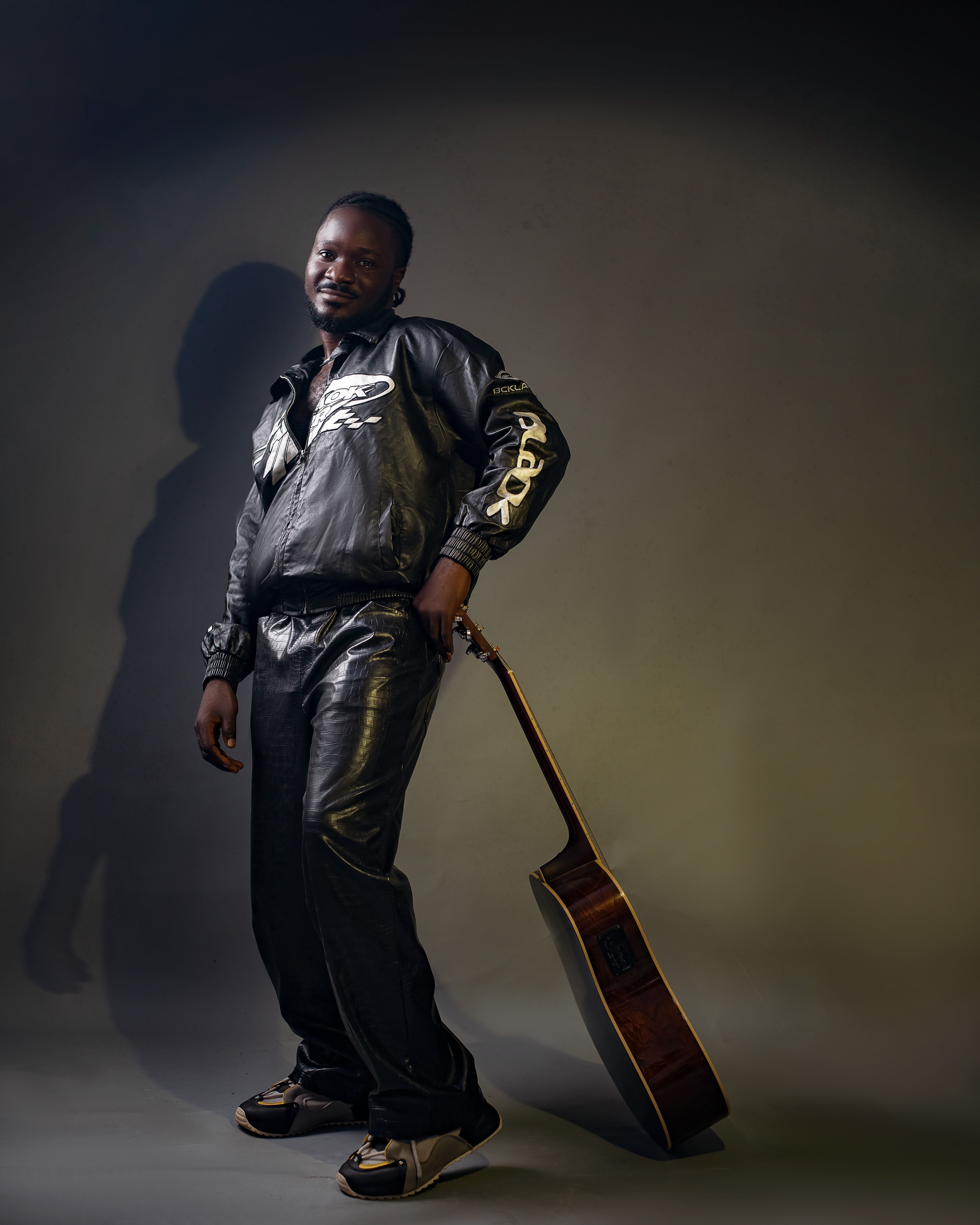Man in leather outfit posing with guitar, exuding confidence and style.