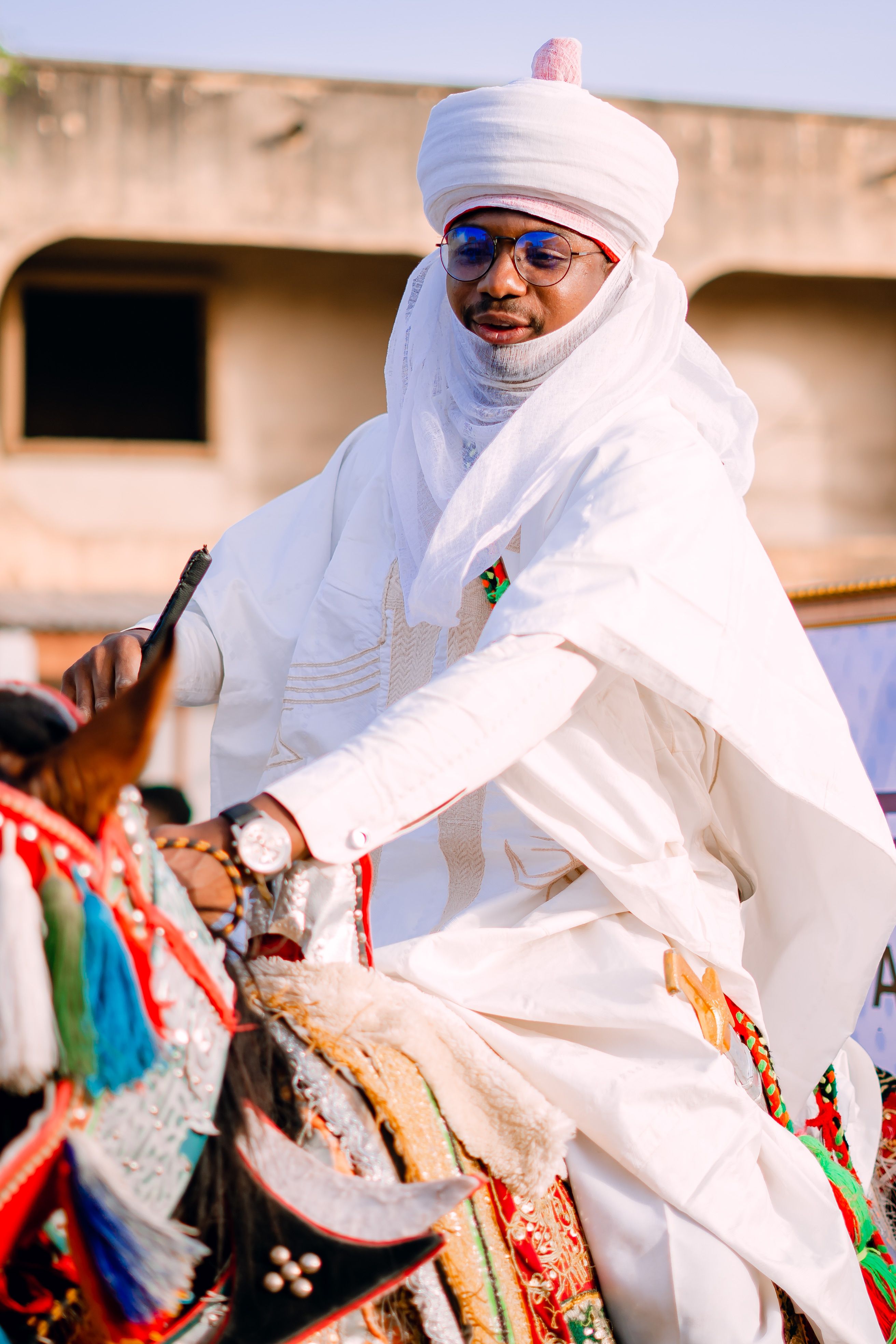 Nigerian Emir in traditional white attire on a colorful horse during a cultural event.