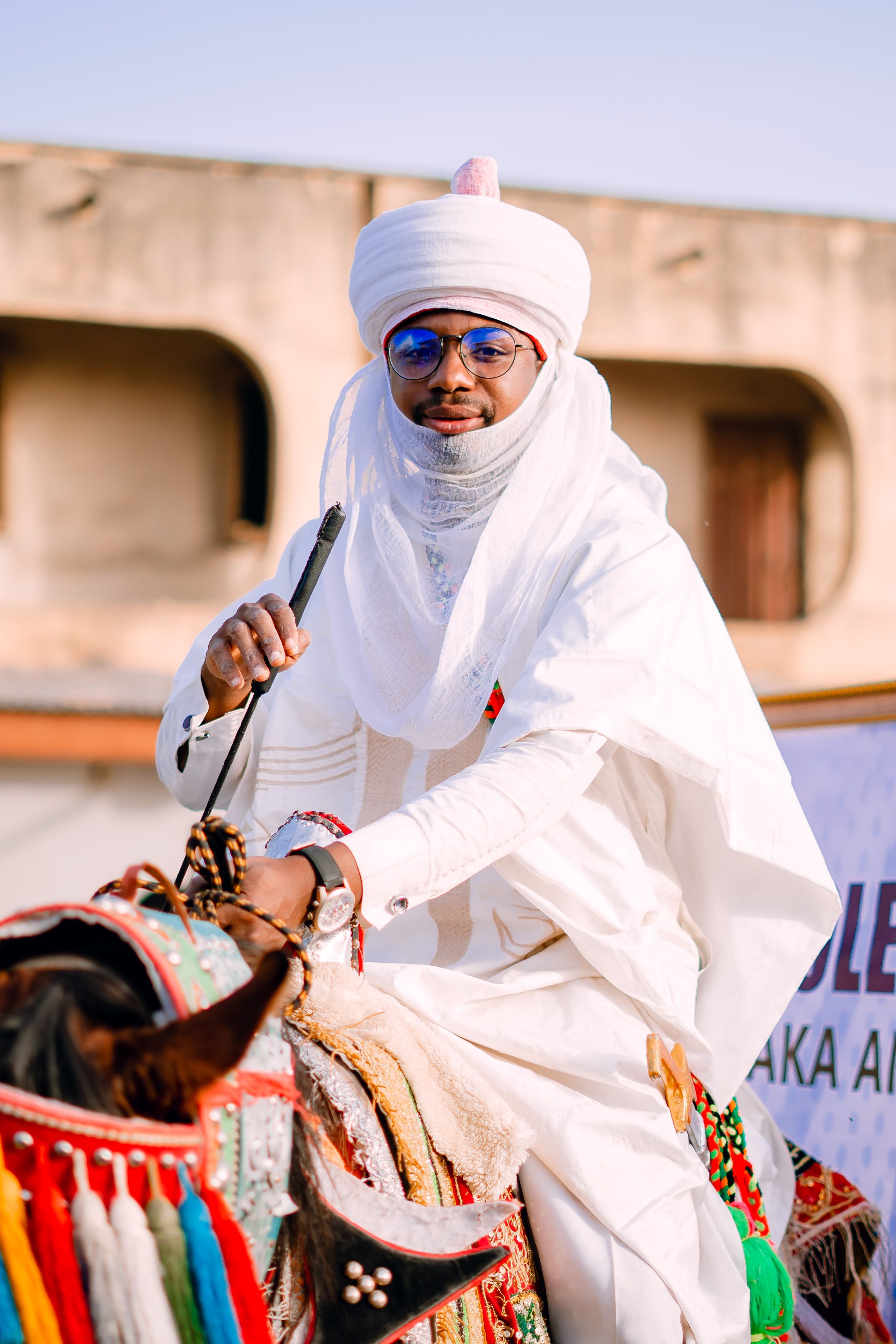 Man in traditional Nigerian attire riding a decorated horse, showcasing cultural heritage.