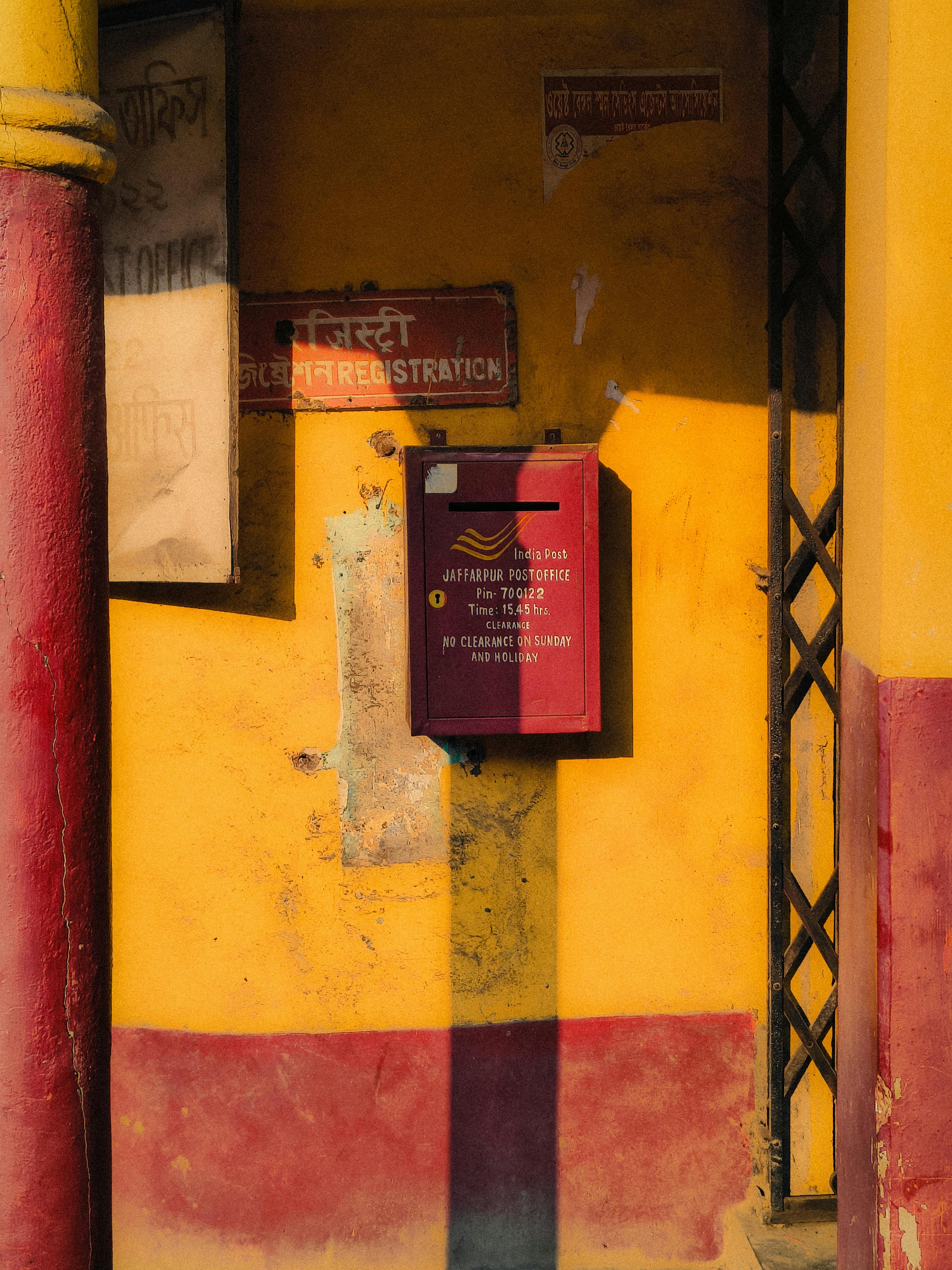 Bright red mailbox against a vivid yellow wall in the afternoon sun in Barrackpore, India.