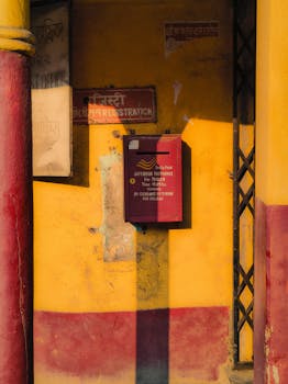 Bright red mailbox against a vivid yellow wall in the afternoon sun in Barrackpore, India.