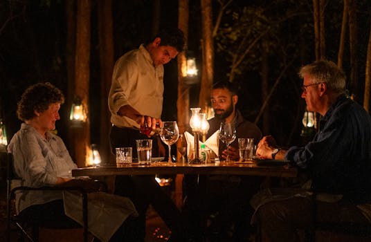 A warm, candlelit dinner among friends in a serene Indian forest setting.