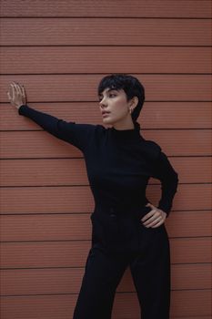 Fashionable woman posing against a wooden wall in a chic black outfit.