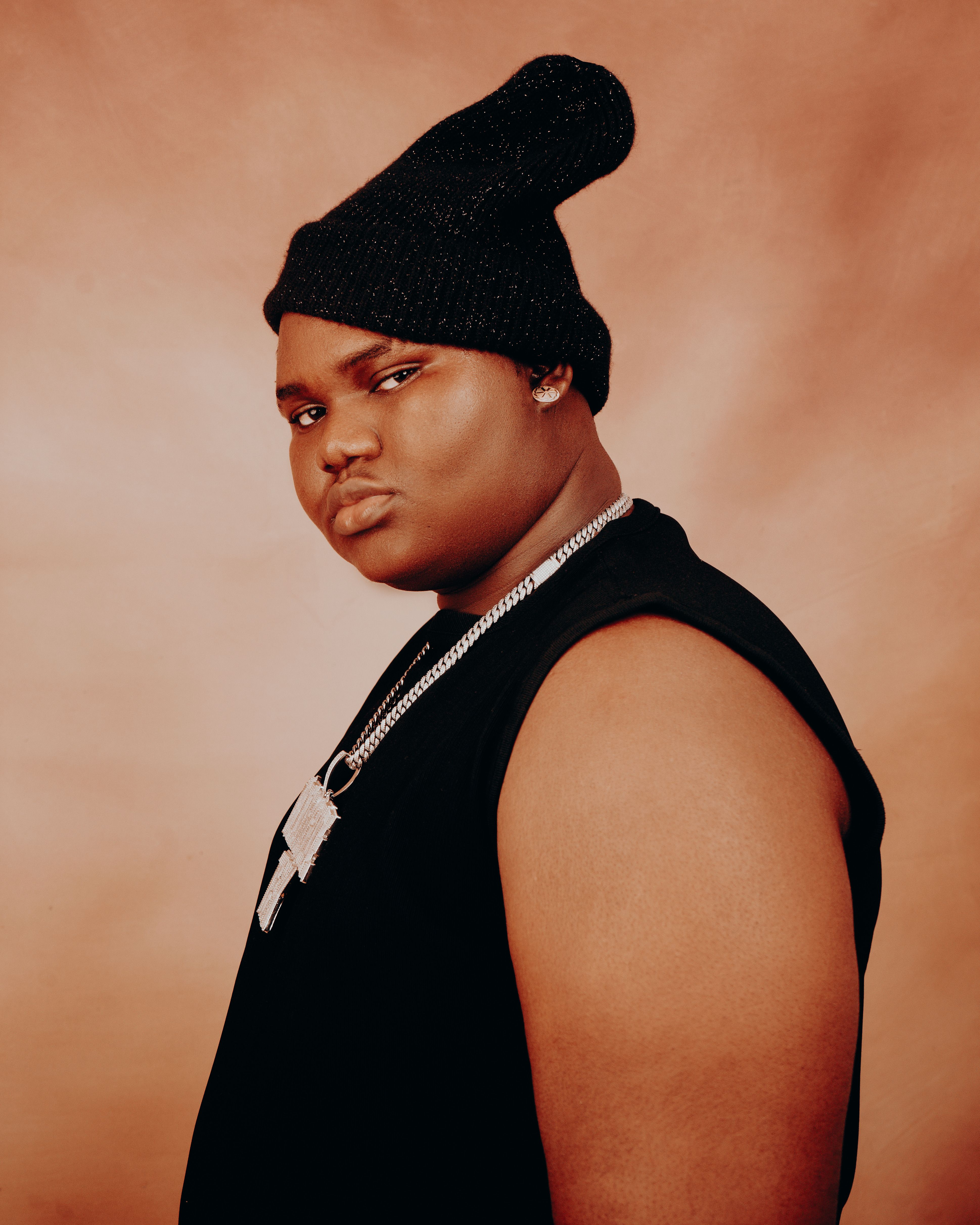 Confident man wearing a beanie and jewelry against a plain background.