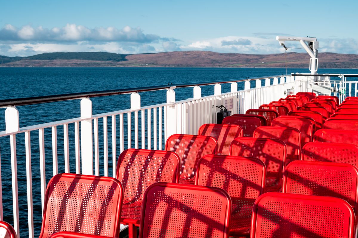 Scaune rosii pe puntea unui ferry scotian, cu coasta in fundal