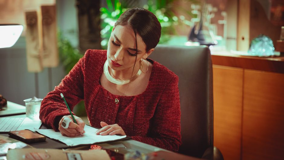 Oura Ring vs Whoop vs Apple Watch: Sleep Tracking Accuracy Showdown A woman in a red blouse focuses on writing at her desk in a cozy office environment.