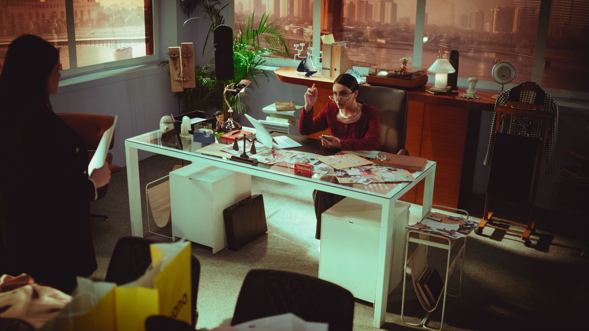 Two women discussing work in a stylish Baghdad office with cityscape view.