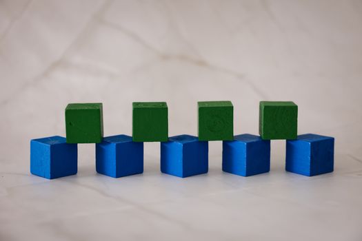 Arrangement of blue and green wooden blocks on a marble surface, creating a playful geometric pattern.