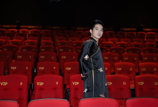 A young man stands confidently in a luxurious VIP cinema with vibrant red seats.