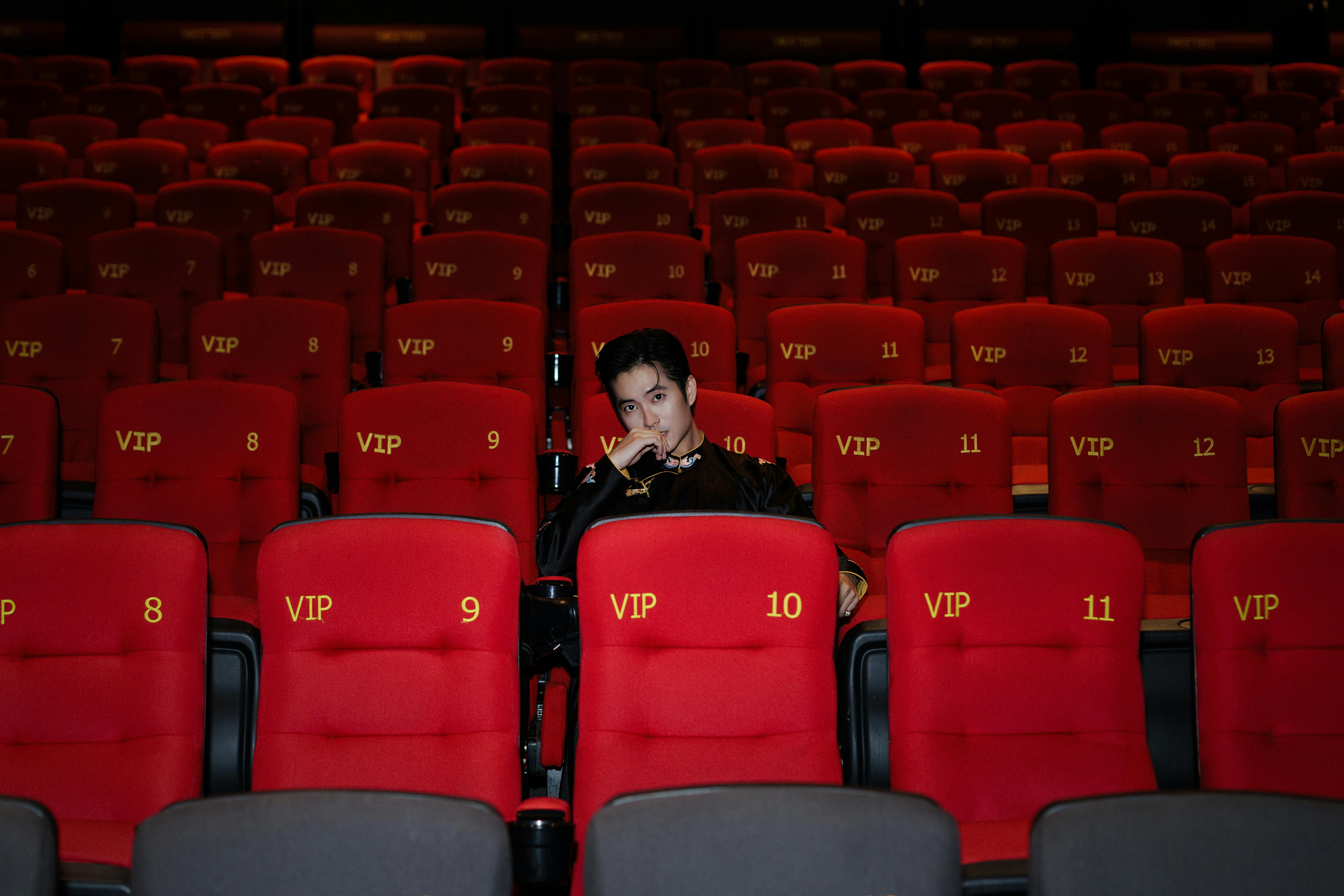 Gratis Una persona está sentada sola en una sala VIP, rodeada de butacas rojas vacías. Foto de stock