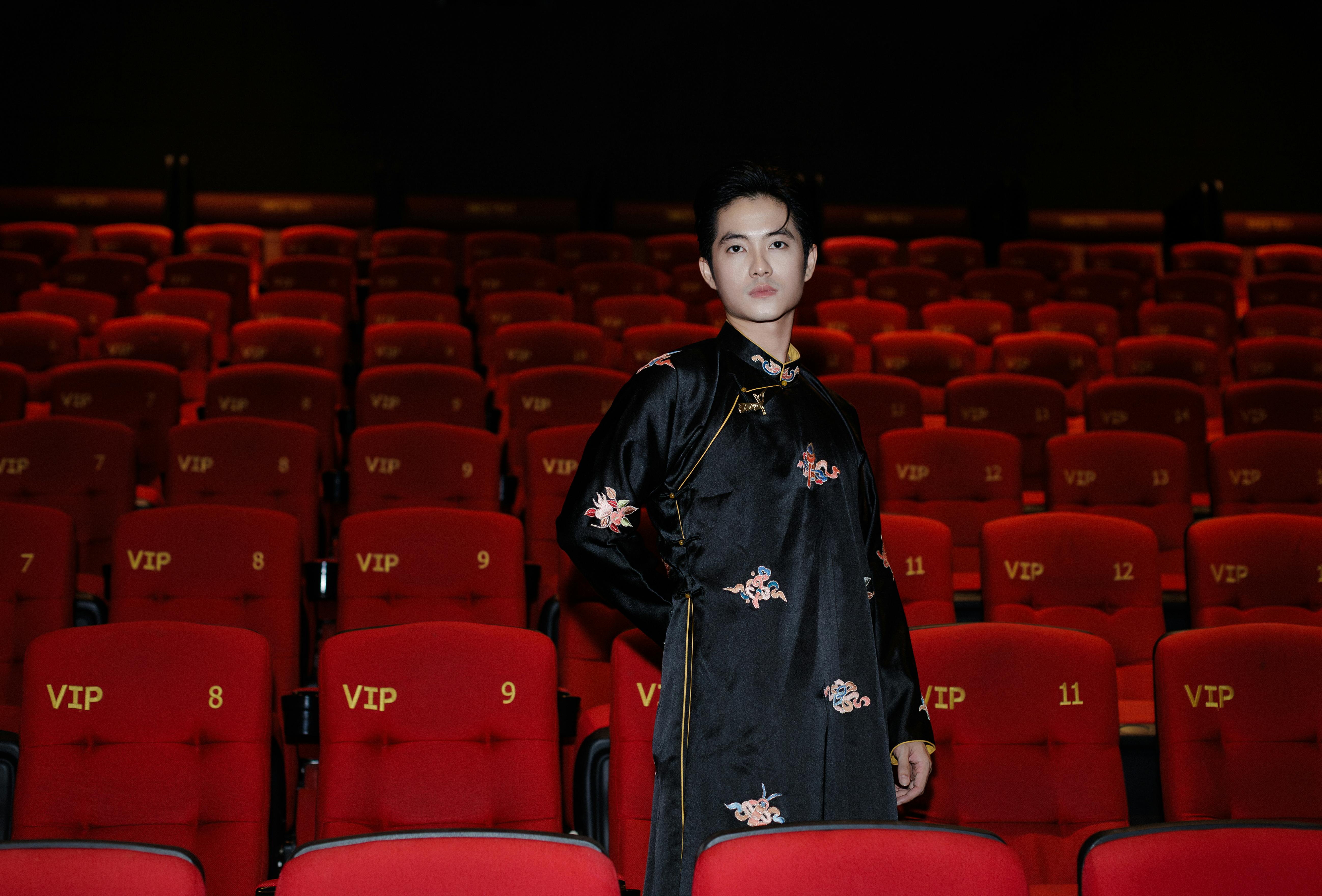 Free Portrait of an Asian man in traditional clothing standing in a VIP cinema with red seats and floral patterns. Stock Photo