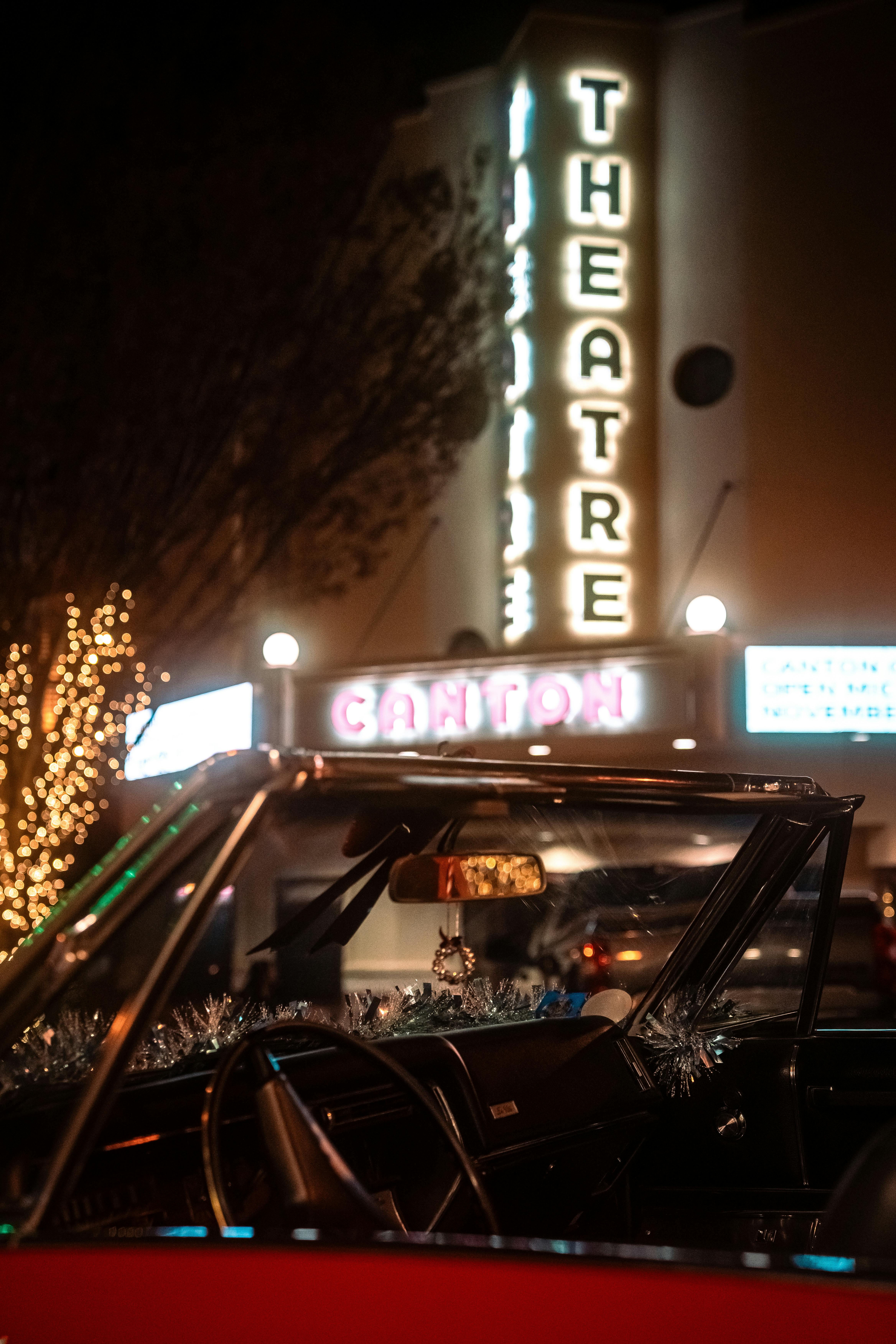 Free A classic convertible parked outside a lit-up theater at night, with holiday decorations visible. Stock Photo