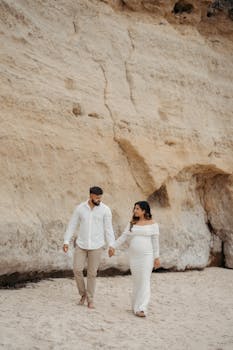 Romantic couple walking on a beach beside rocky cliffs, hand-in-hand.