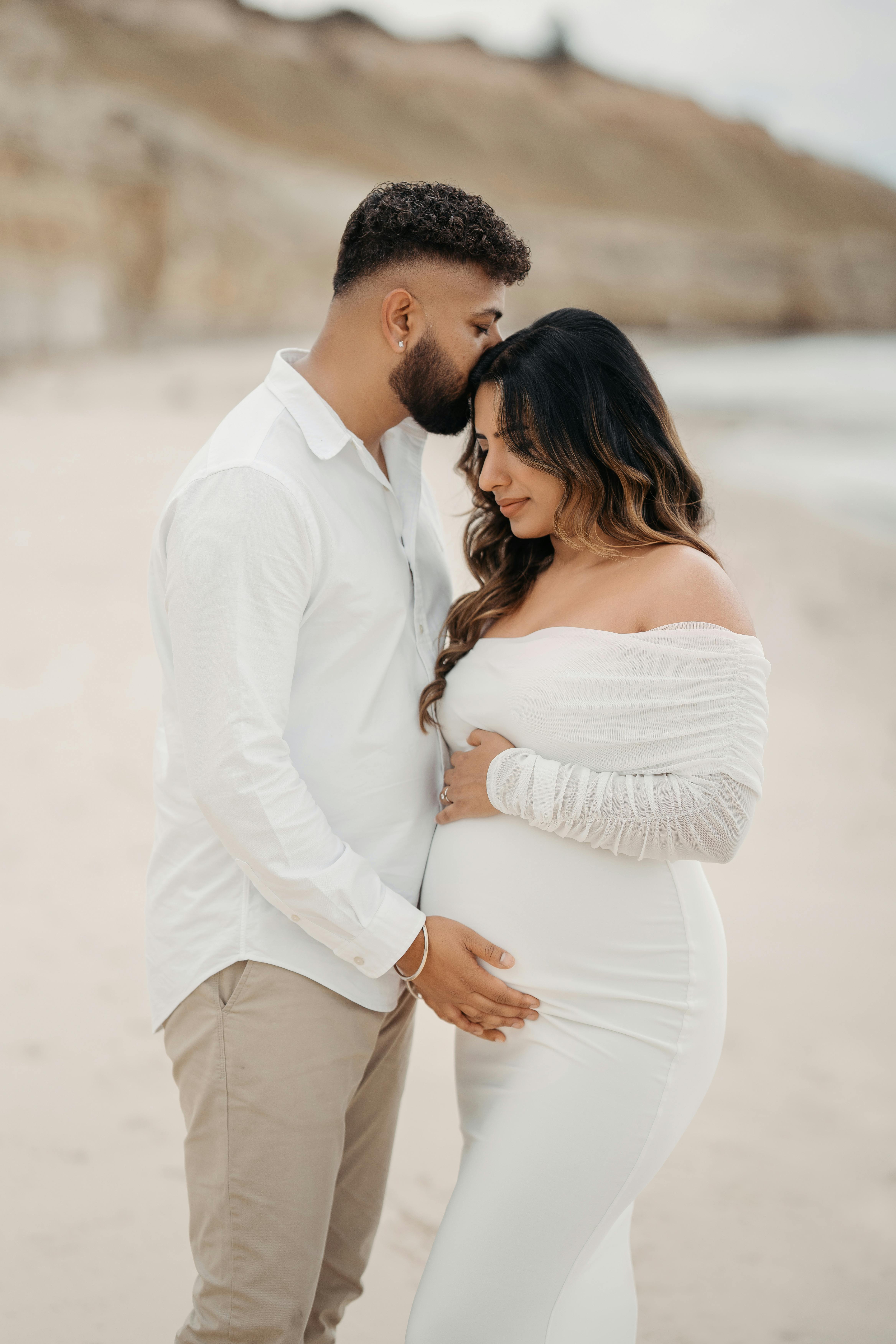 Loving couple embracing on a beach, focused on maternity joy and serenity.