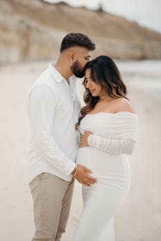 Loving couple embracing on a beach, focused on maternity joy and serenity.