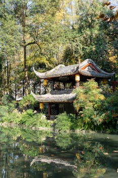 Beautiful pavilion surrounded by lush greenery reflecting in a serene pond.