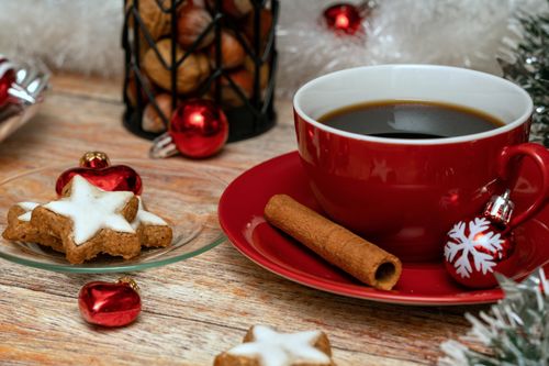 Free Red cup of coffee with cinnamon stick, star cookies, and holiday decor on a wooden table. Stock Photo