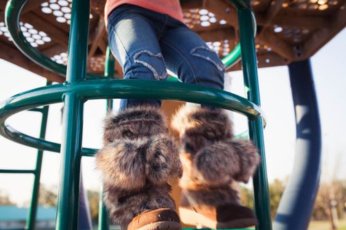 Free Low angle view of a child playing outdoors at a playground wearing furry boots and jeans. Stock Photo