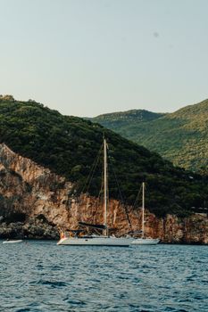 A serene yacht anchored by lush, rocky hills in Corfu, Greece, under a clear summer sky.