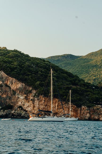 A serene yacht anchored by lush, rocky hills in Corfu, Greece, under a clear summer sky.