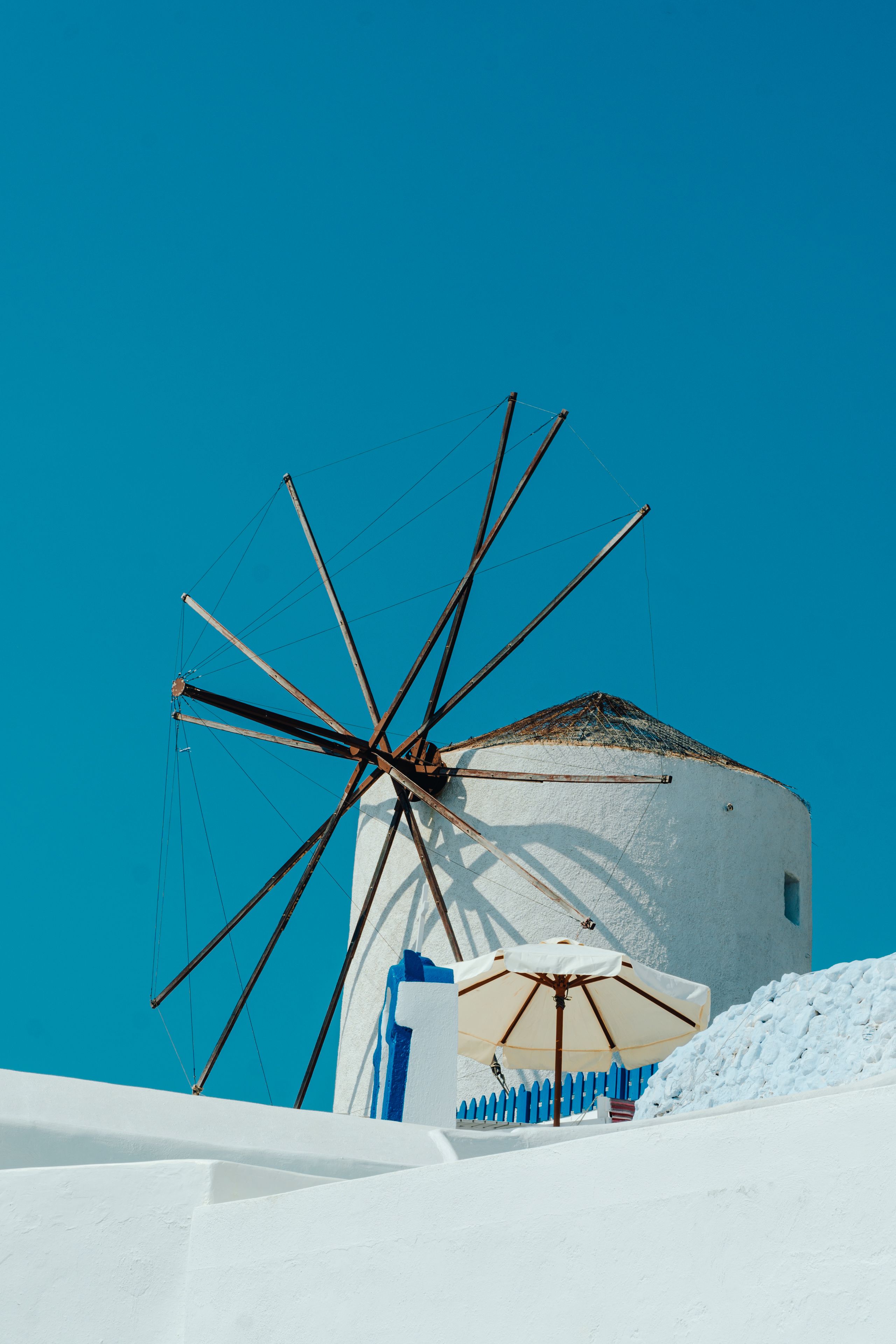 Iconic white windmill in Fira, Santorini, against a vibrant blue sky, featuring traditional Greek architecture.