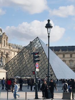 The iconic glass Pyramid at the Louvre Museum in Paris with bustling tourists.