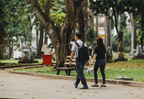 Free A couple enjoys a walk through a lush park in Ho Chi Minh City, Vietnam, surrounded by trees and pathways. Stock Photo
