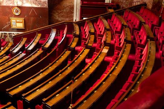A luxurious interior view of a legislative chamber with curved red seating and wooden desks.