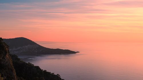 Free A picturesque sunset over a calm sea with a silhouetted hill, offering a serene view. Stock Photo
