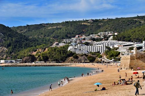 Free Beautiful beach scene in Sesimbra, Portugal with vibrant coastline and hillside buildings. Stock Photo