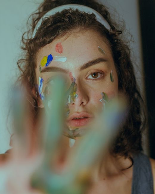 A woman with face paint looks at the camera, showcasing artistic expression and creativity.