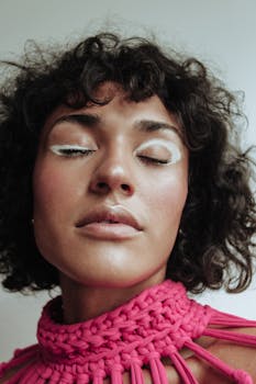 A close-up portrait of a woman with eye-catching creative makeup and a vibrant pink top.