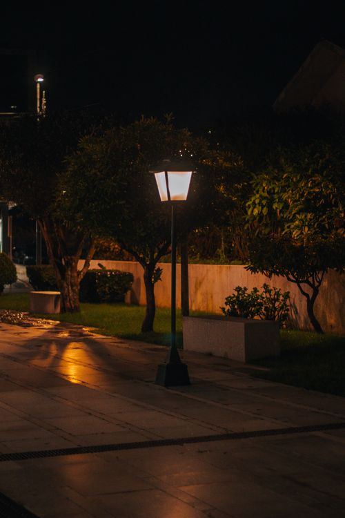 Free Serene nighttime scene with a lit street lamp casting a warm glow on a quiet pathway. Stock Photo