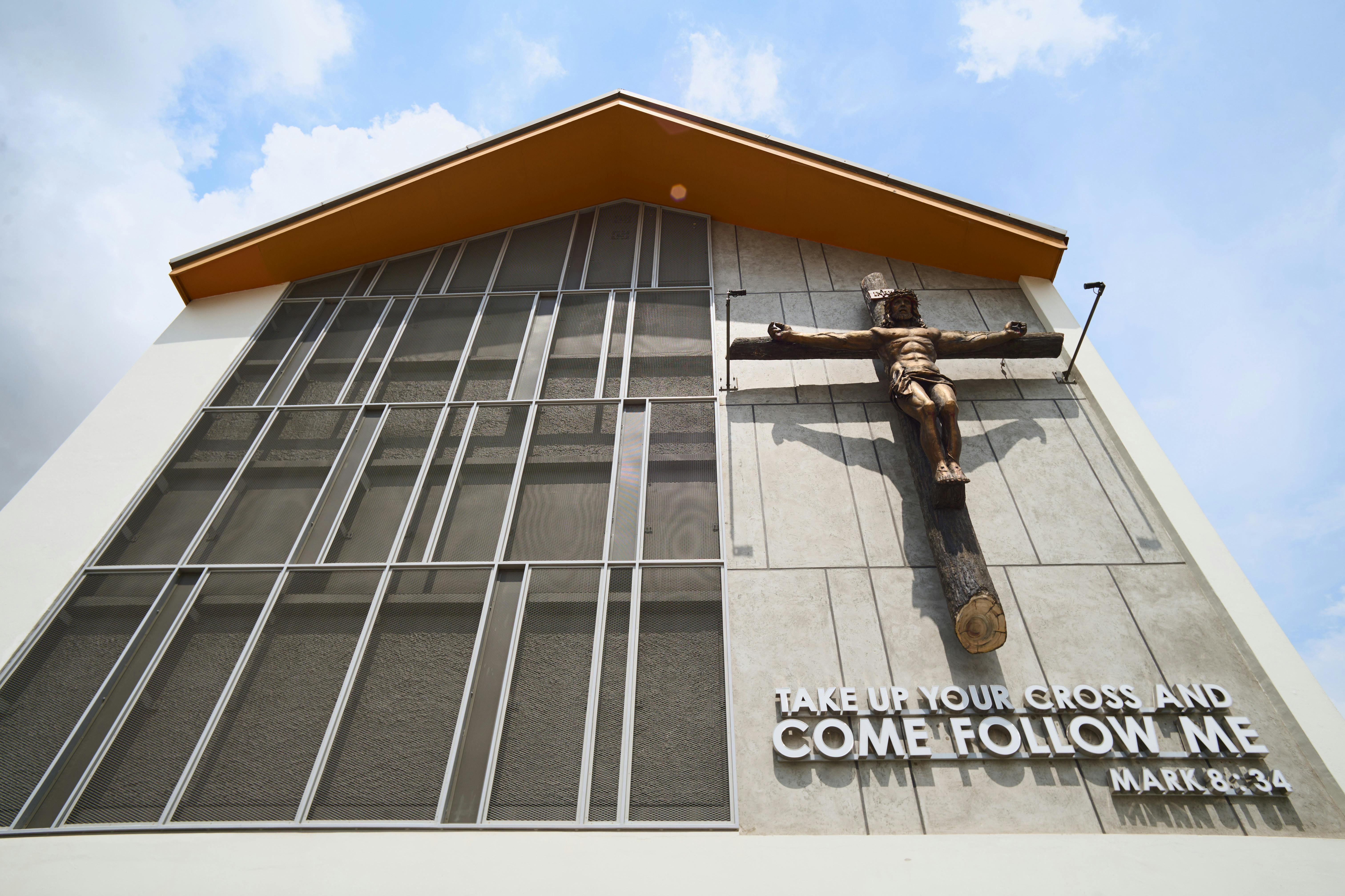 A modern church facade featuring a crucifix and an inspirational quote from Mark 8:34.