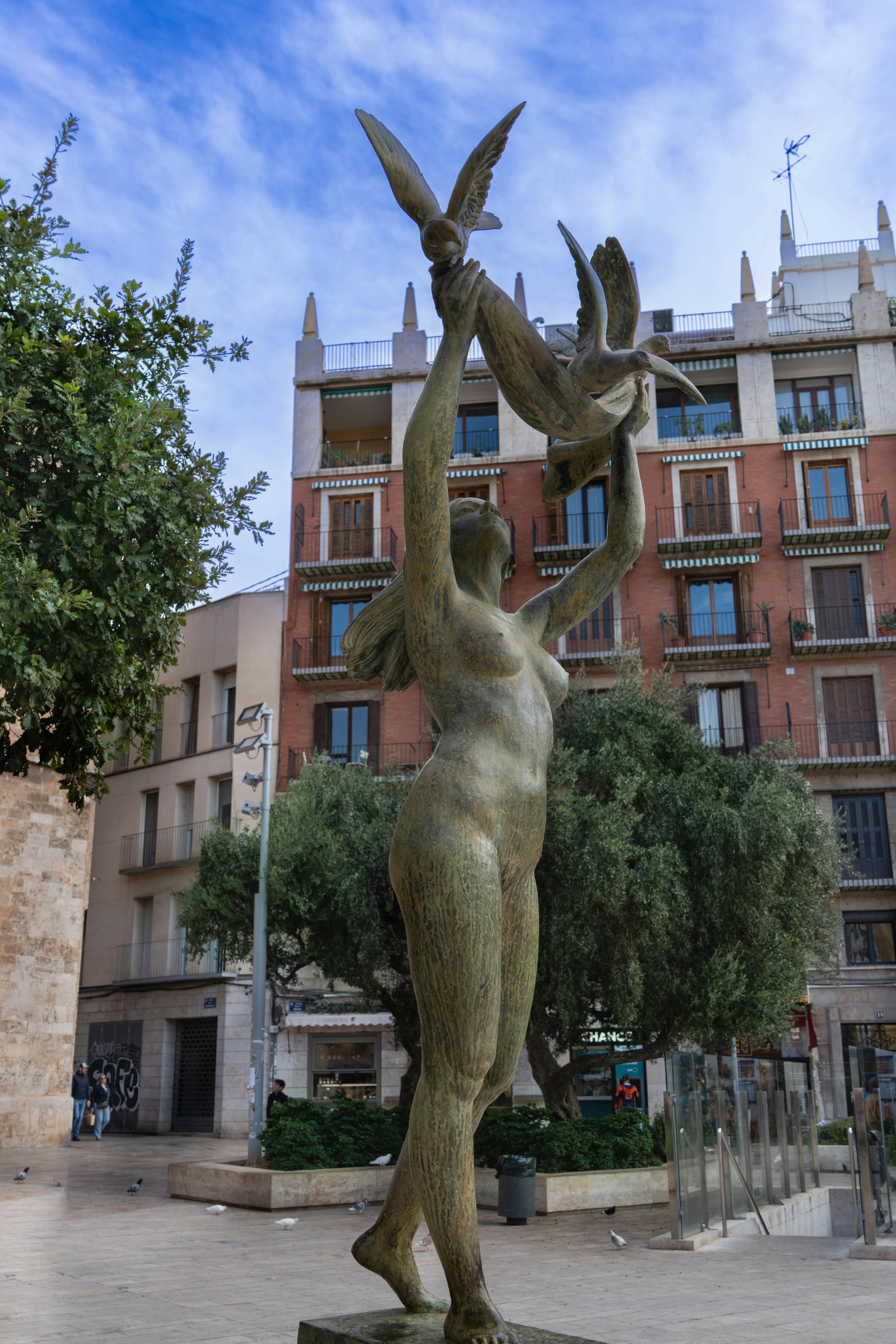 A bronze sculpture of a woman releasing birds in a vibrant city plaza in Valencia, Spain.