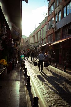 A lively urban street scene with pedestrians walking under the warm glow of a sunset.