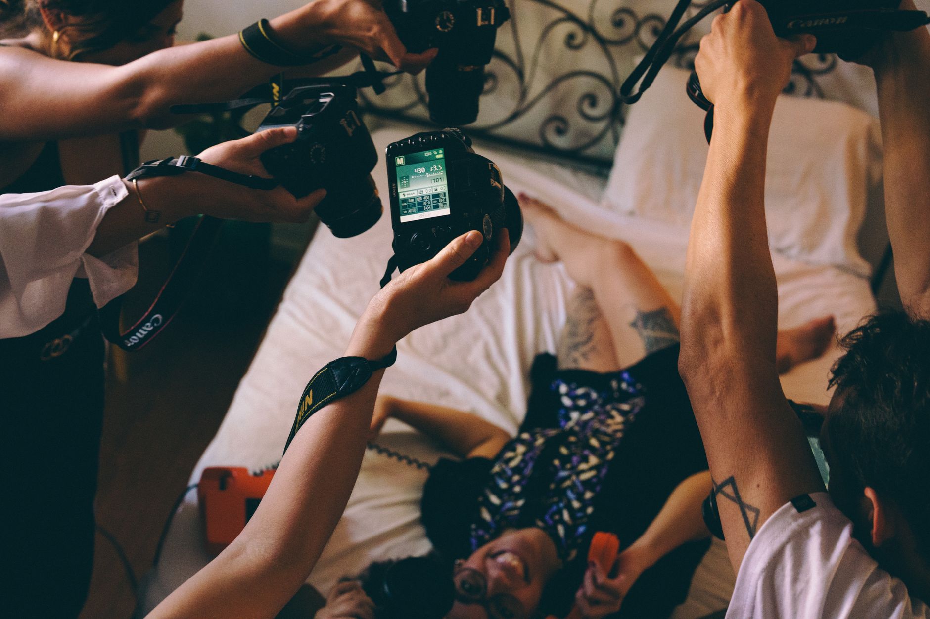 Group of photographers capturing a model lying on a bed indoors.