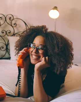 Cheerful woman enjoying a conversation on a vintage rotary phone in a cozy bedroom setting.