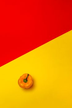 A vibrant yellow bell pepper on a red and yellow color block background.