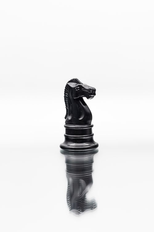 Free A black knight chess piece stands on a reflective surface, symbolizing strategy and intellect. Stock Photo