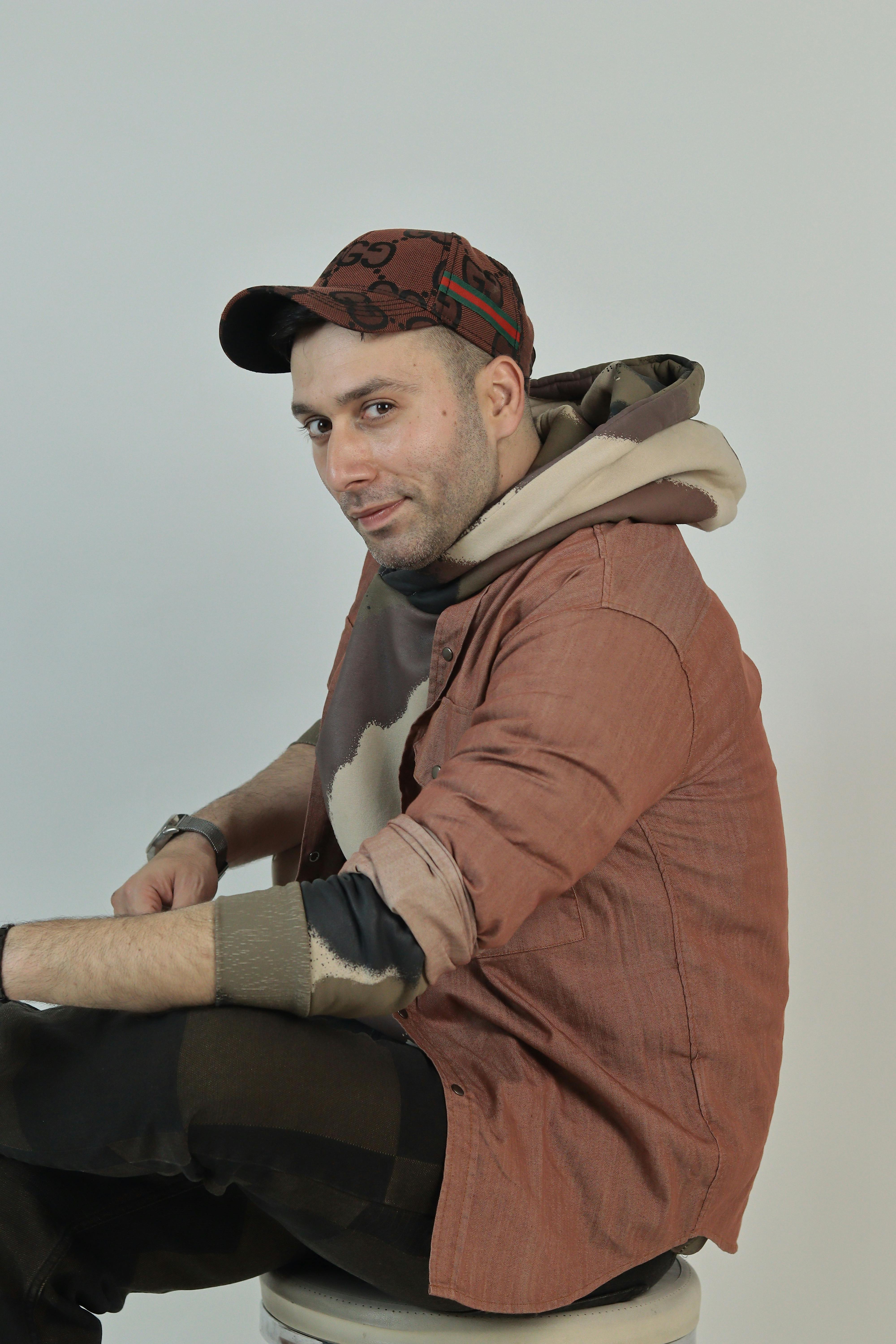 De franc Un jove relaxat amb gorra i dessuadora amb caputxa seu còmodament amb un fons neutre. Foto d'estoc