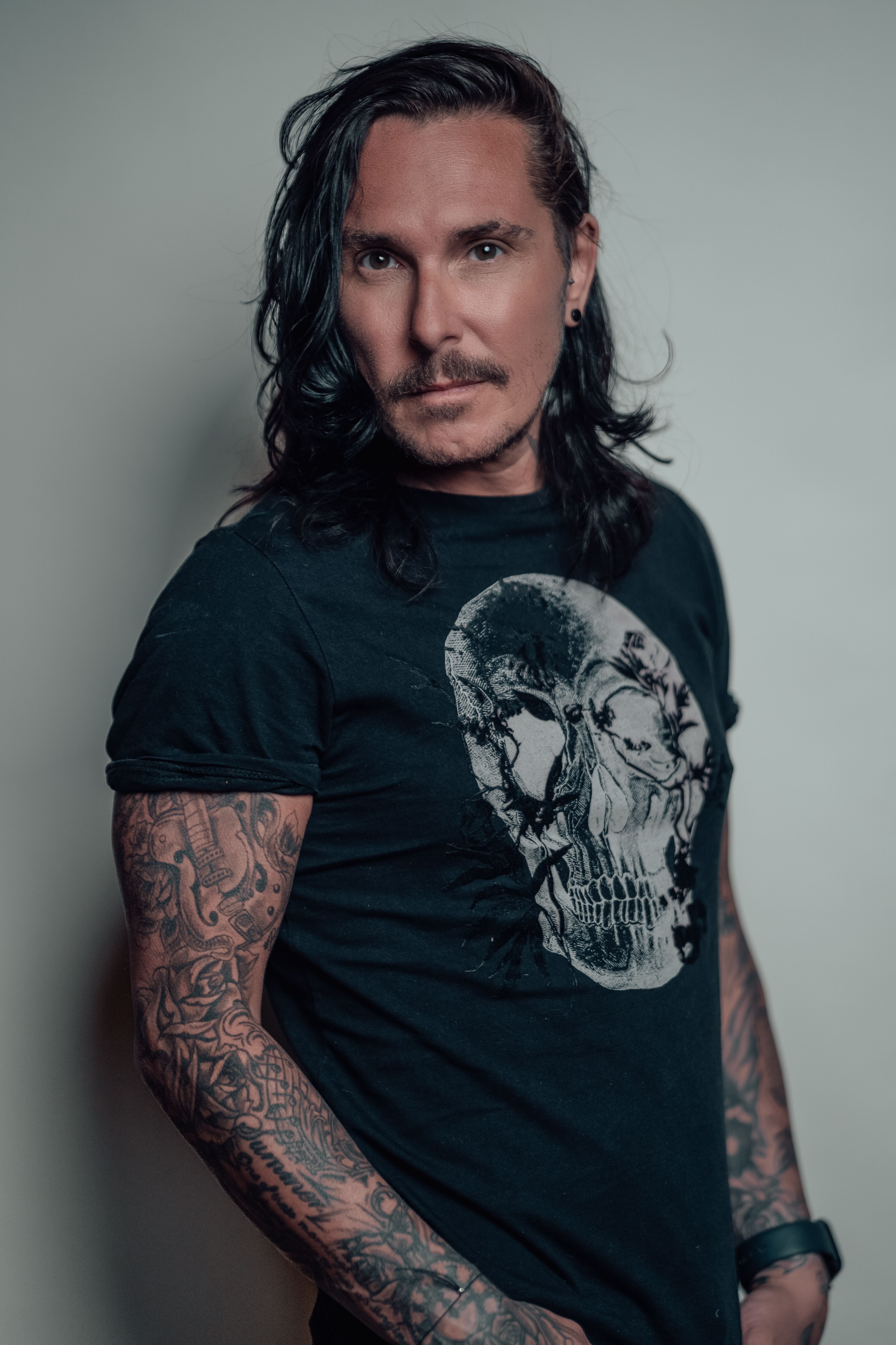 Confident man with tattoos and long hair wearing a skull t-shirt. Ideal for rock music themes.