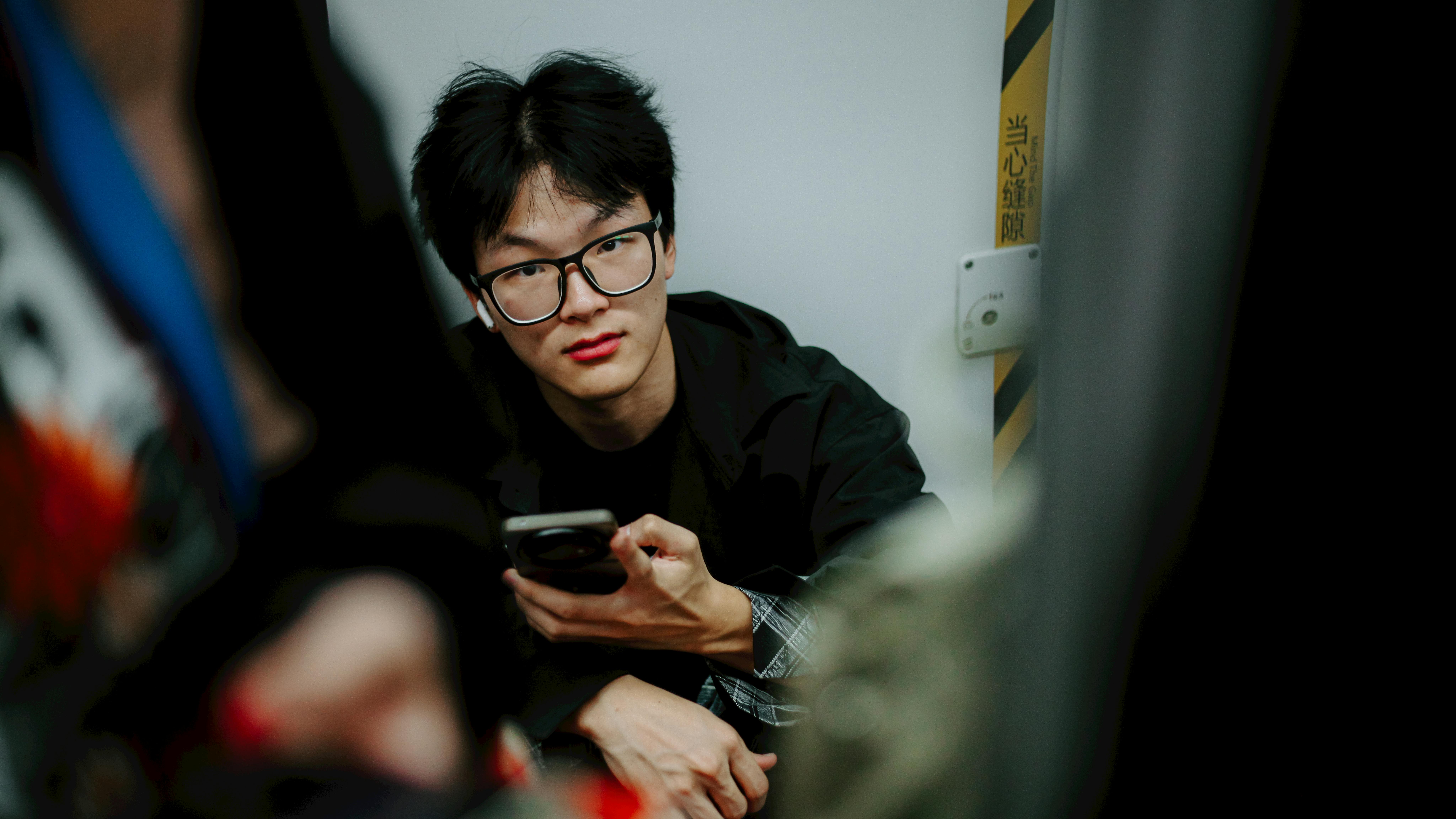 Gratis Potret seorang pria muda memegang telepon pintar di dalam ruangan, menatap langsung ke kamera. Foto Stok