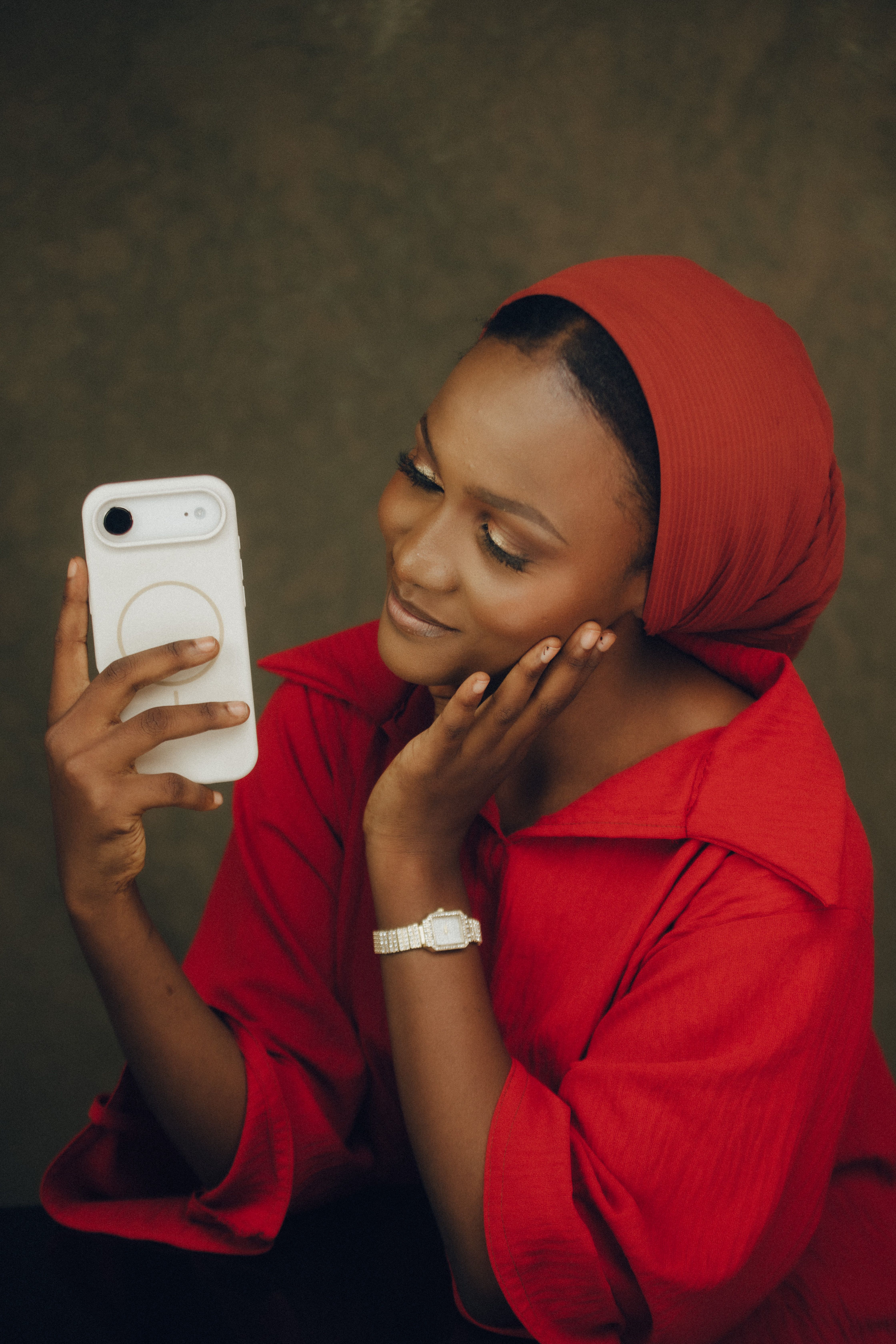 Smiling woman in red clothing taking a selfie with her phone, showcasing casual elegance.