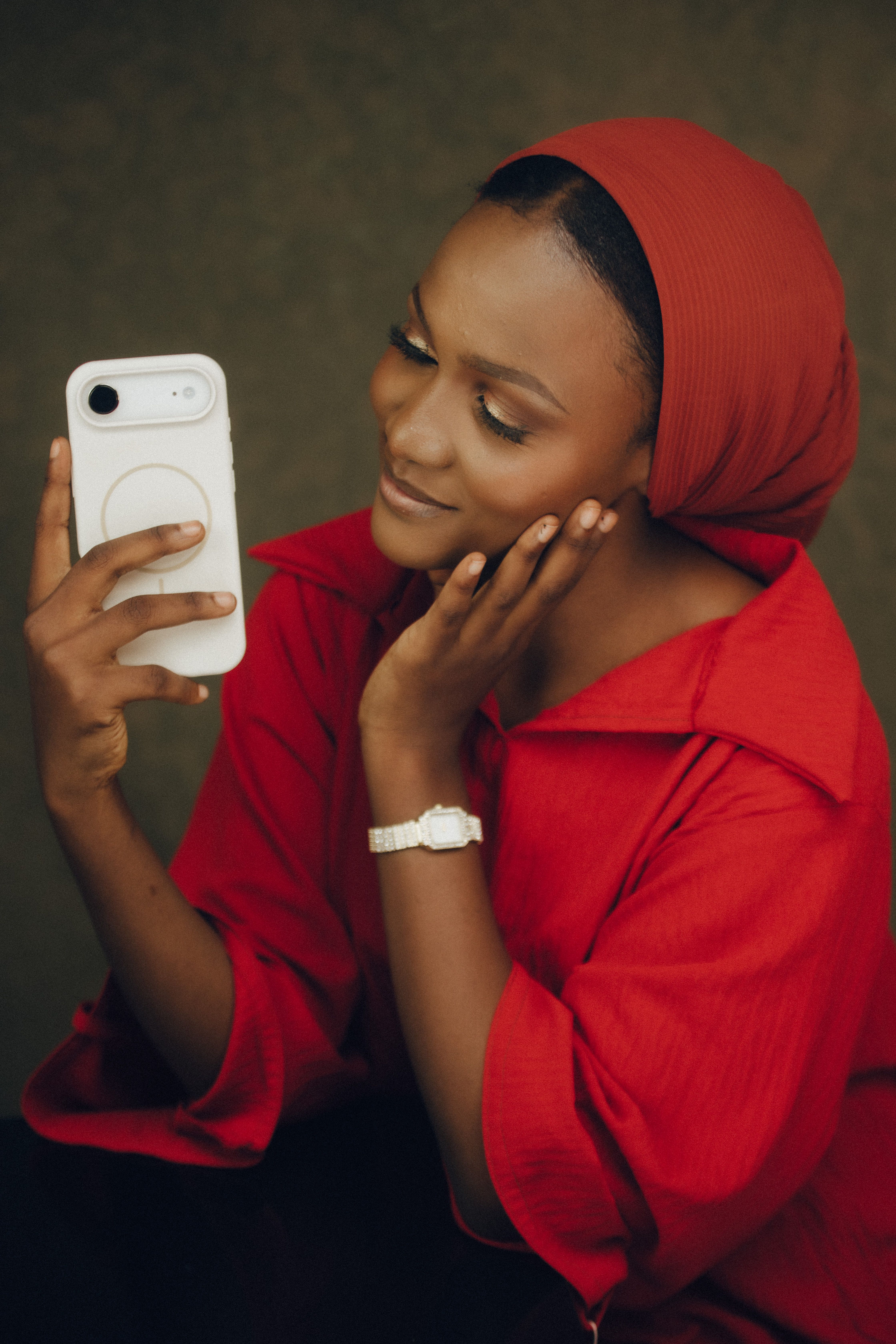 Young woman in red hijab taking a selfie with a smartphone indoors.