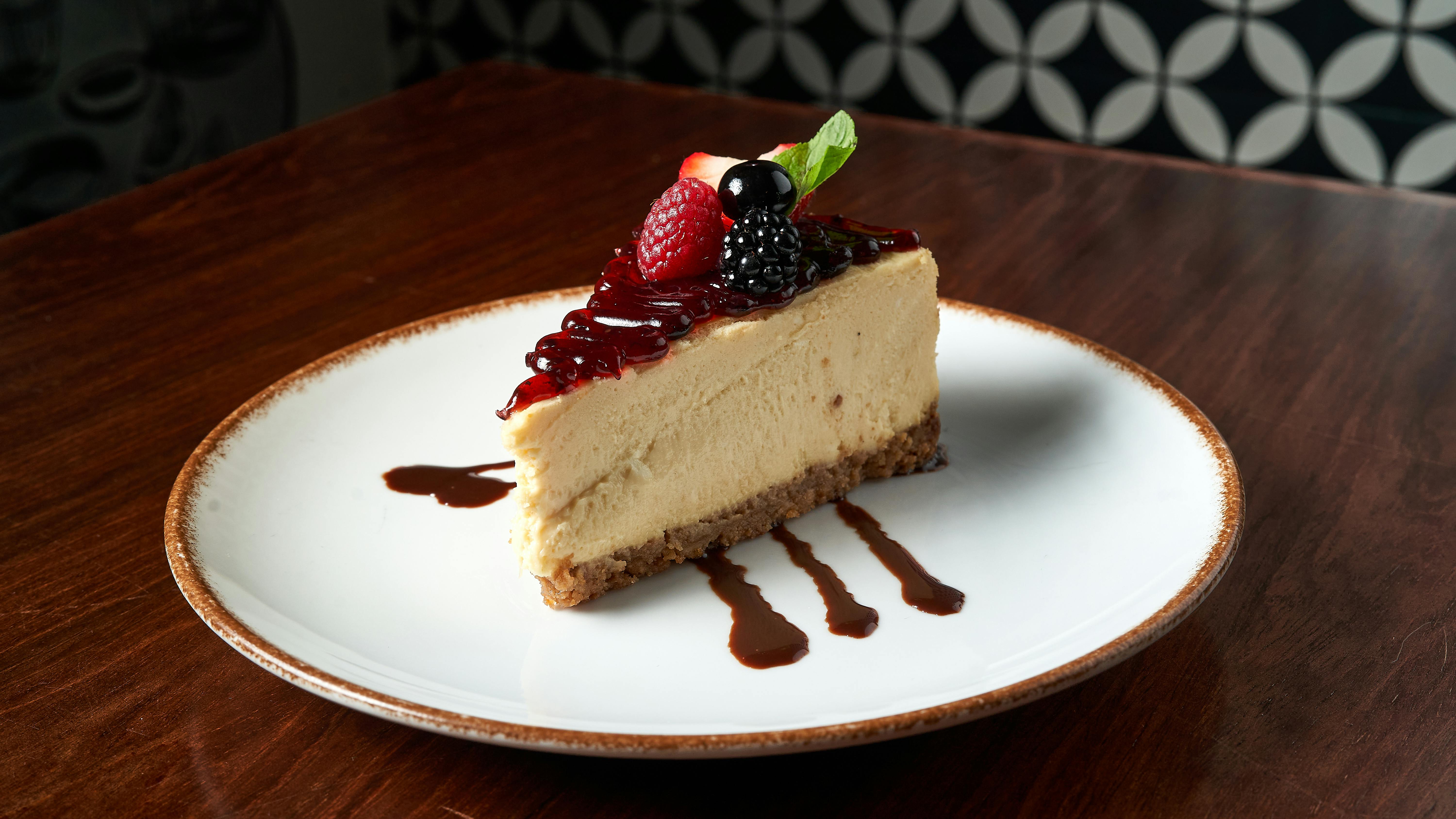 Slice of cheesecake topped with fresh berries and sauce on a plate.