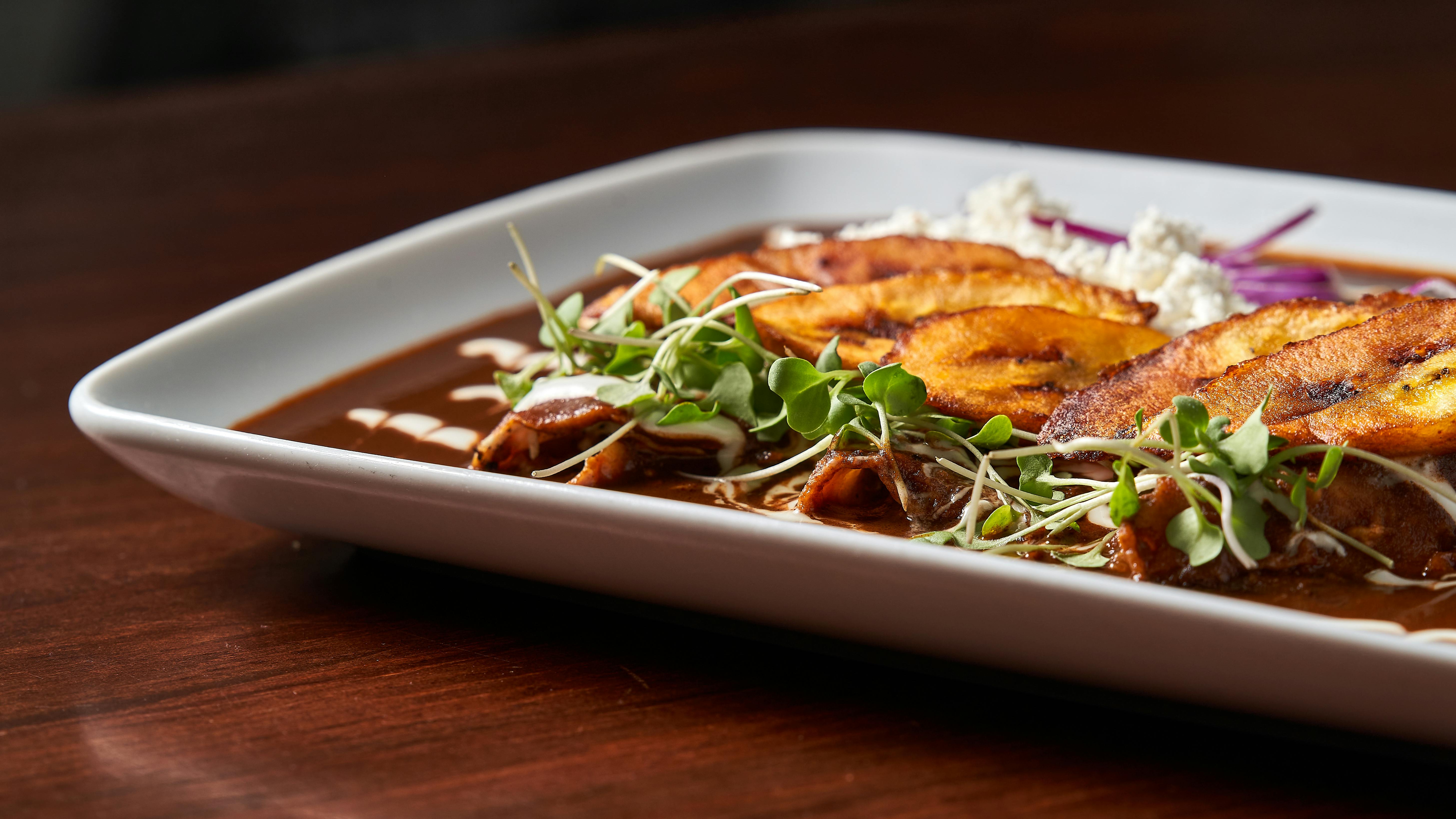 A gourmet dish with plantains, microgreens, and creamy sauce on a white plate.