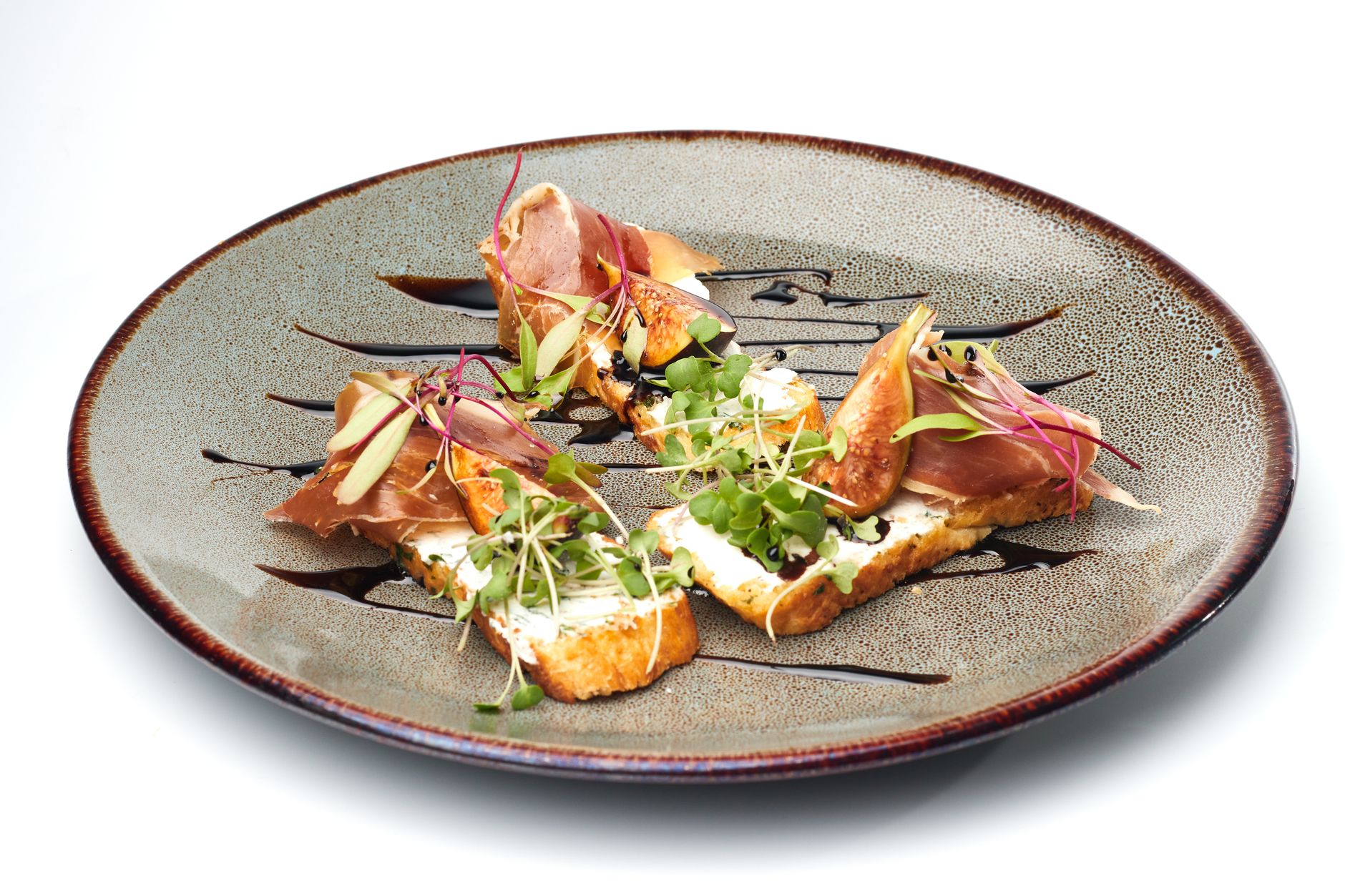 Elegant crostini topped with prosciutto, figs, and microgreens on a ceramic plate.