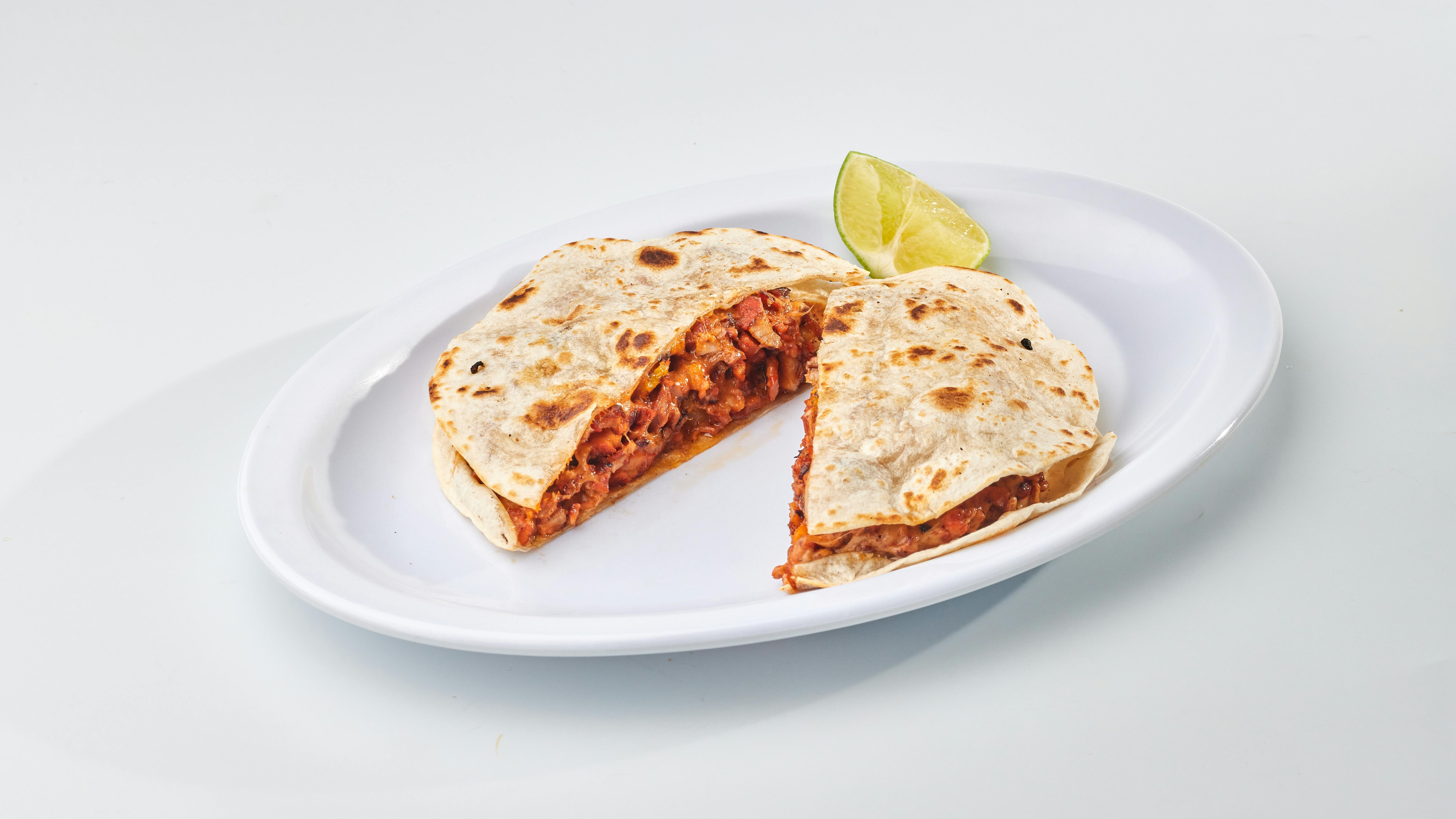 Appetizing Mexican quesadilla with cheese served on a white plate, accompanied by a lime wedge.