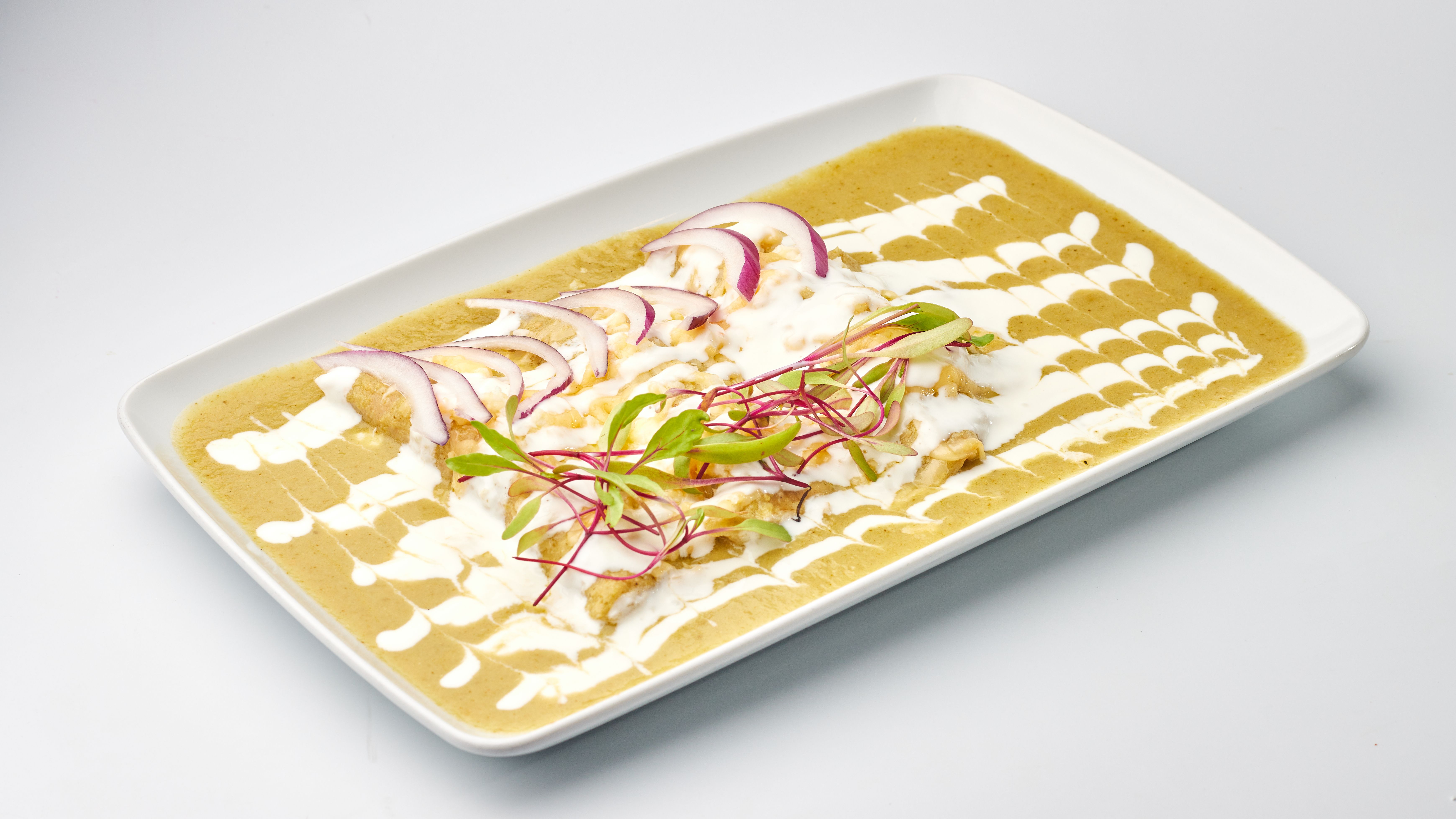 Delicious enchiladas garnished with sliced onions and fresh greens on a white platter.